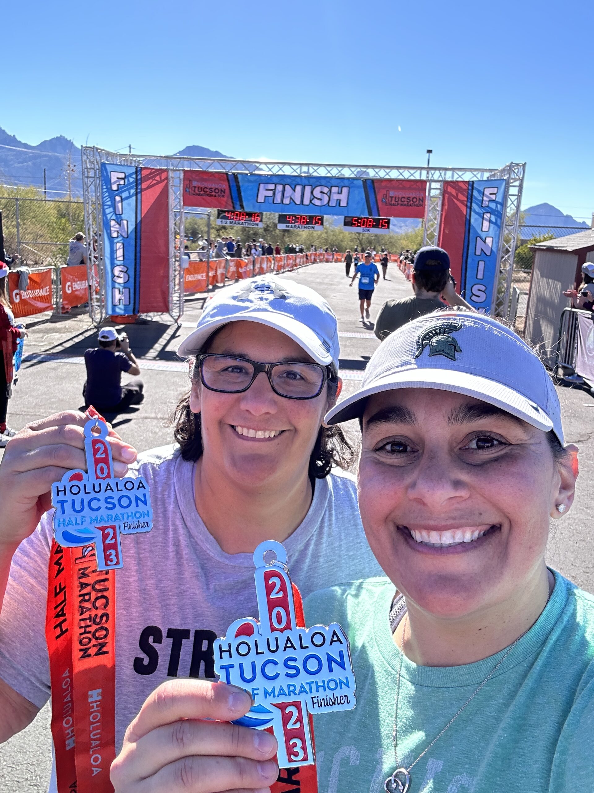 Two women smiling holding half marathon race medals at the finish line